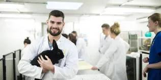 A vet student holding a rabbit with other students and staff in the background