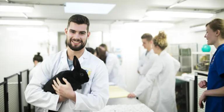 A vet student holding a rabbit with other students and staff in the background