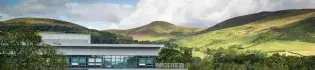 A view of green hills in the sun with clouds and a building in the foreground