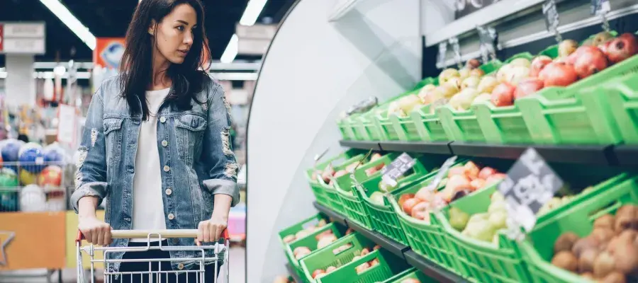 A woman pushing a trolley looks at vegetables in a supermarket.