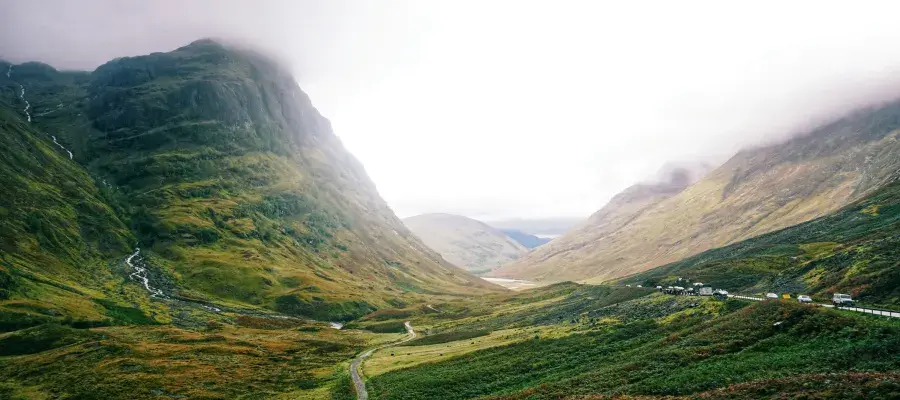A view of Scottish mountain landscape featuring a river and road, with low cloud.