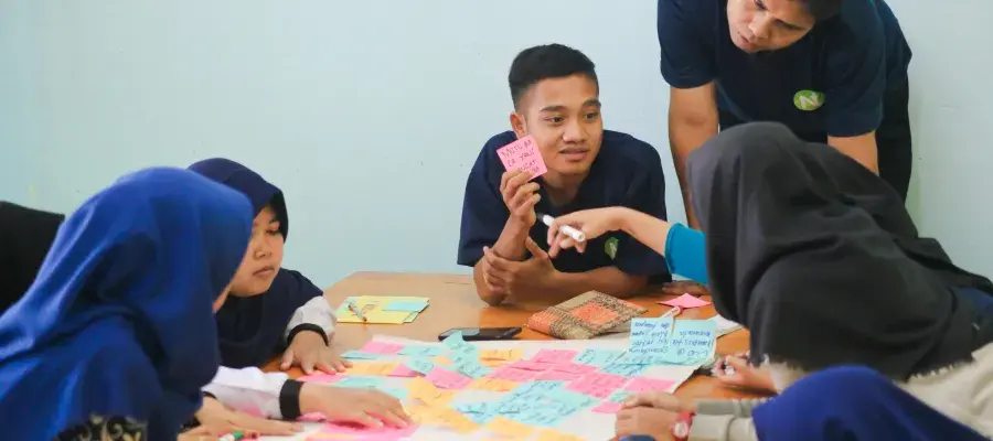 A group of young people sit around a table, engaged in a team task