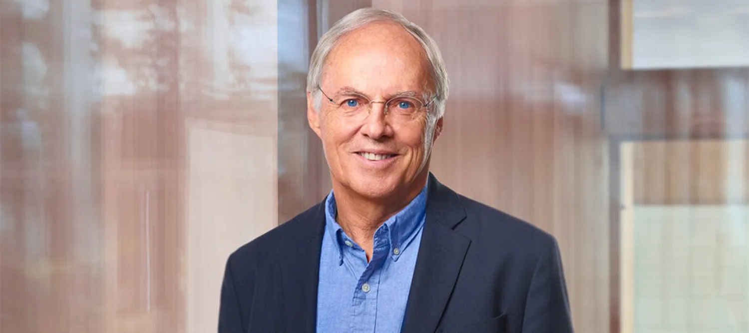 Professor Hans Clevers wearing a dark blue suit and standing in front of a glass wall