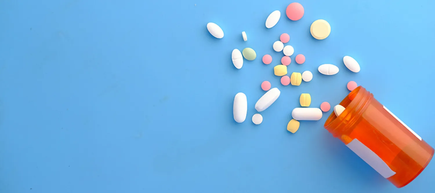 open brown container lying on its side with an assortment of coloured tablets spilling out