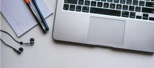 image of laptop next to notepad, earpods and pens
