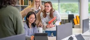 Three students in a library looking at a tablet device