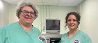image of two females in green scrub tops standing next to an anaethesia machine and smailing to the camera