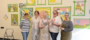 A group of art students stand in front of the mural they have painted