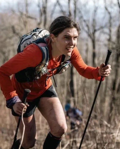 woman in forest setting walking determinedly uphill using walking poles