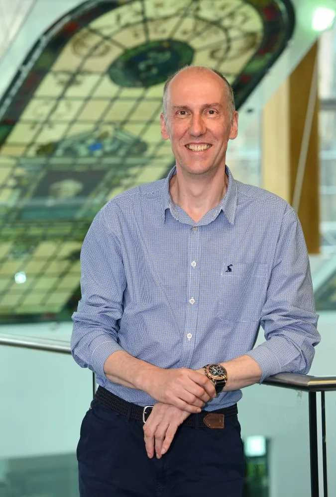 Professor Farquharson standing in front of colourful glass window at the Vet School.