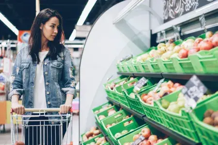 A woman pushing a trolley looks at vegetables in a supermarket.