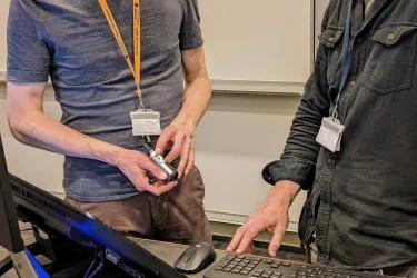 A student with a yellow lanyard explaining how to use a mic to a lecturer
