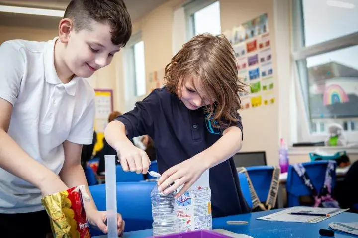Two school children pour sugar into a bottle of water