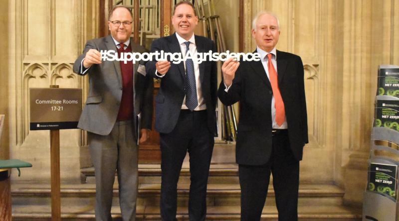 George Freeman MP, Charlie Dewhirst MP and Defra minister Daniel Zeichner stand on a flight of steps carrying a sign in support of agricultural science.