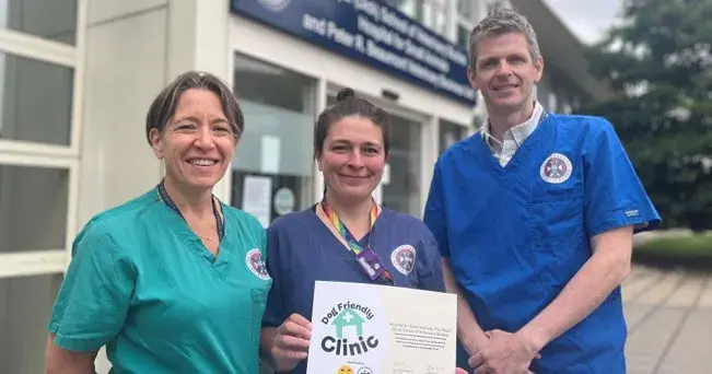 three people in clinical scrubs standing outside the Hospital for Small Animals holding a certificate and smiling to the camera