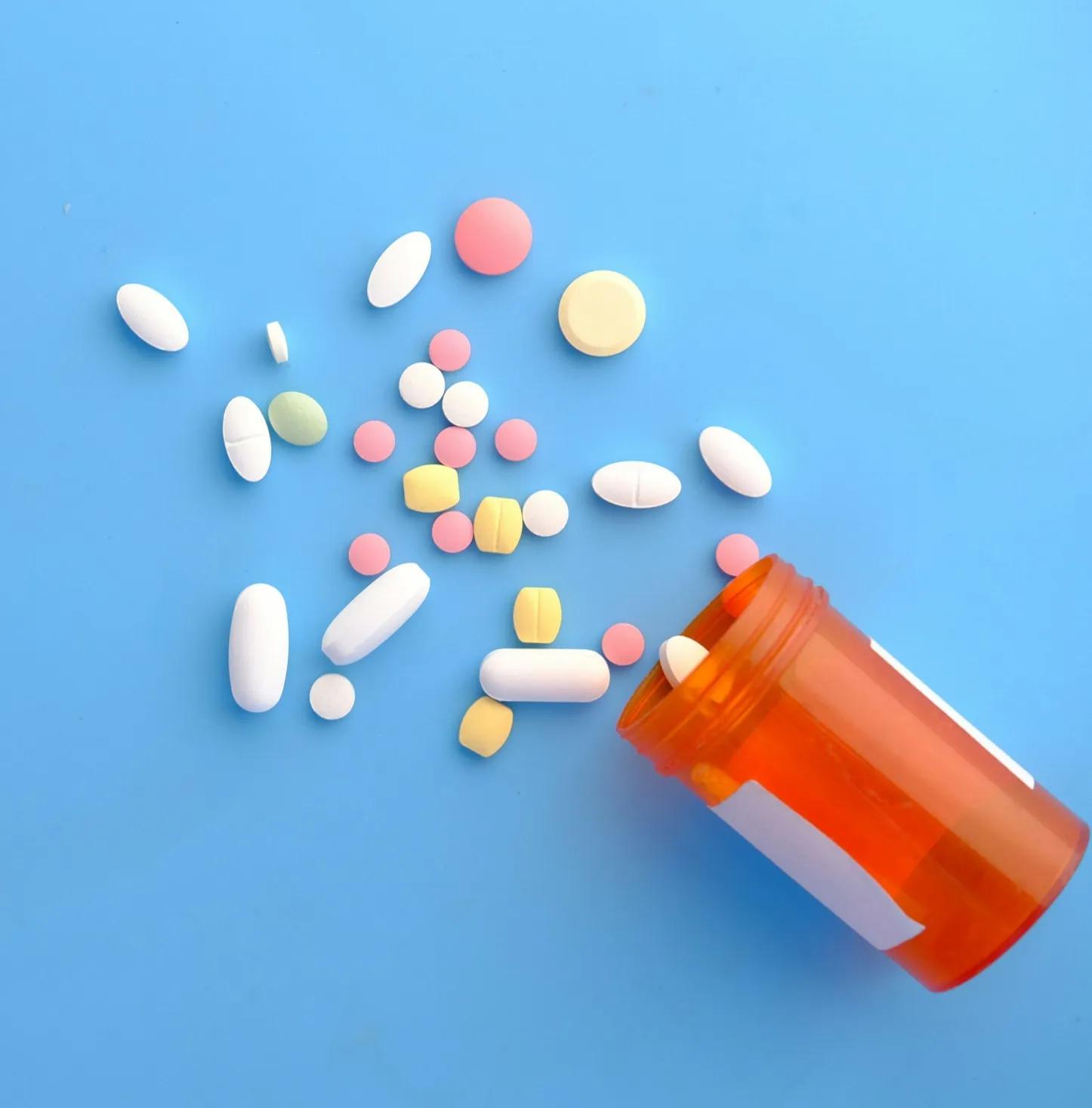 image of plastic container on side with a variety of tablets spilling from it