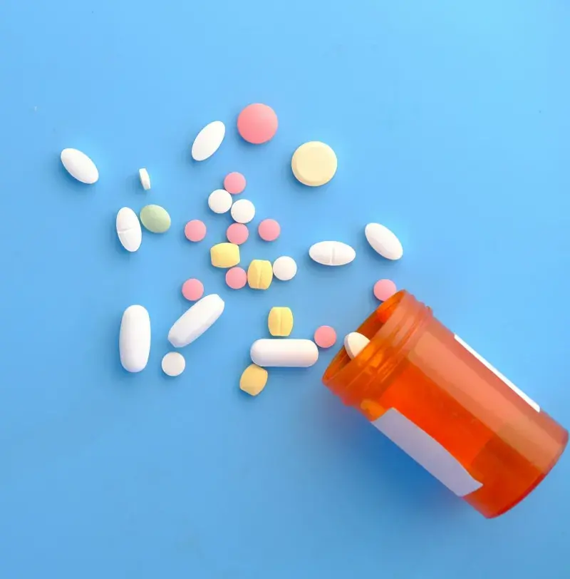 image of plastic container on side with a variety of tablets spilling from it
