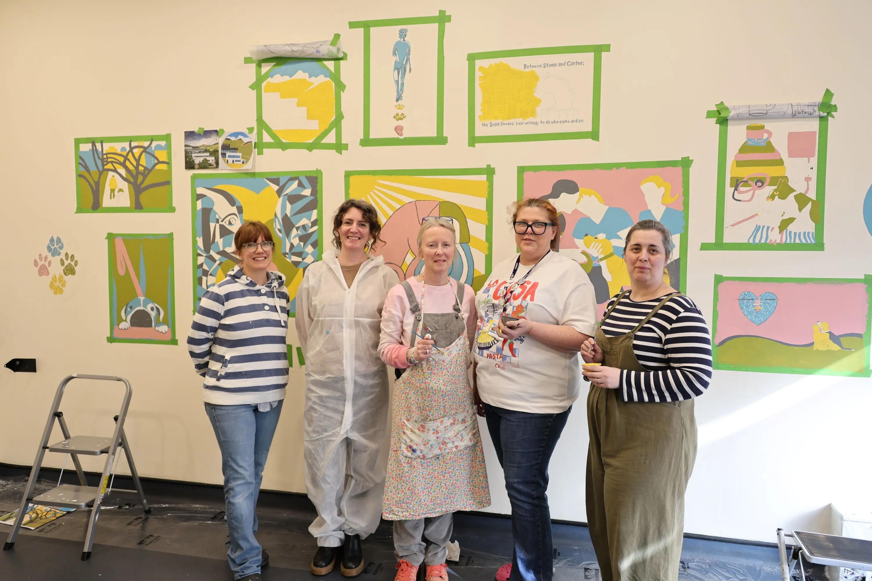 A group of art students stand in front of the mural they have painted