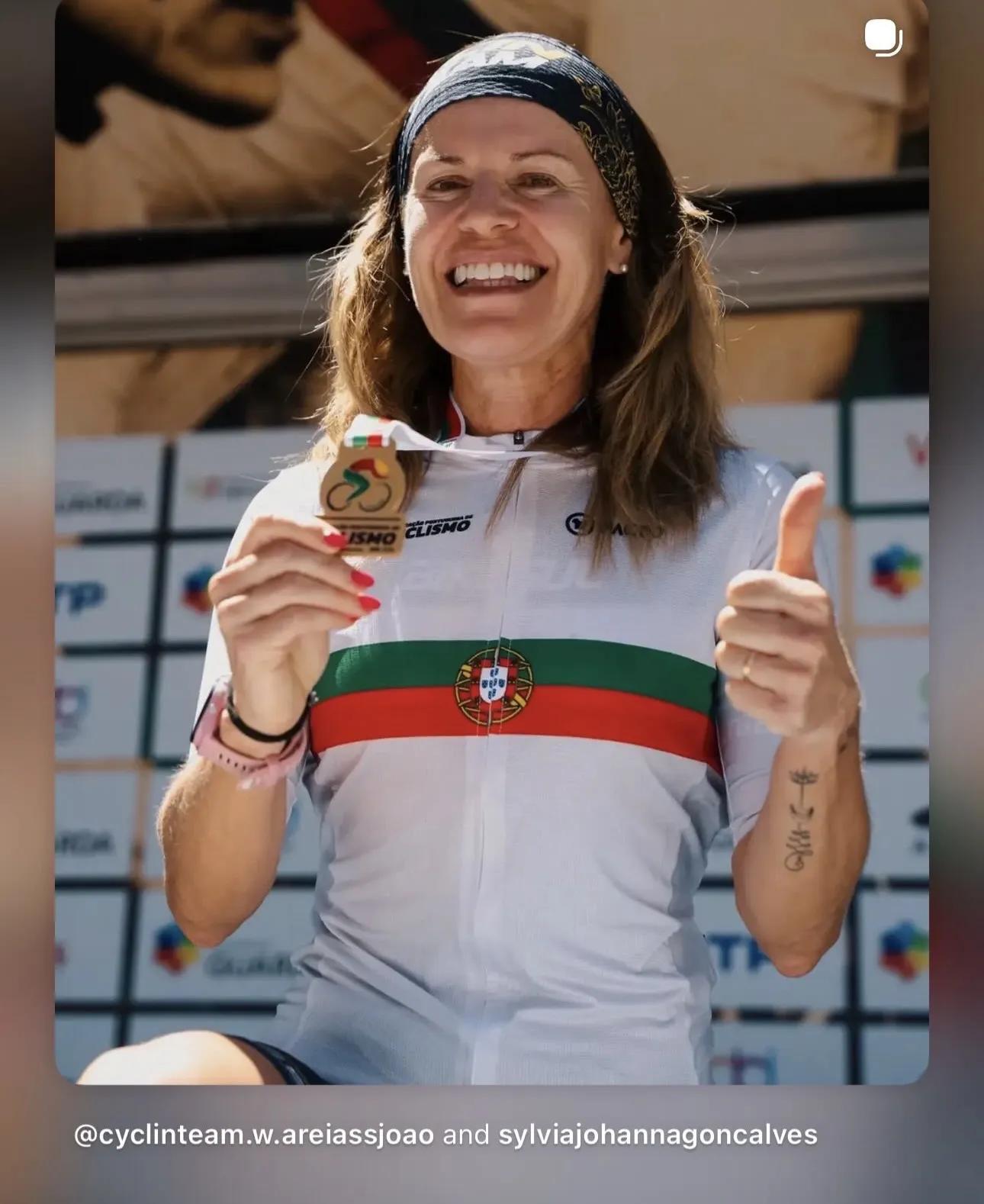 Sylvia Read holding up a medal and giving a thumbs up while smiling. The caption reads "@cyclinteam.w.areiassjoao and sylviajohannagoncalves".