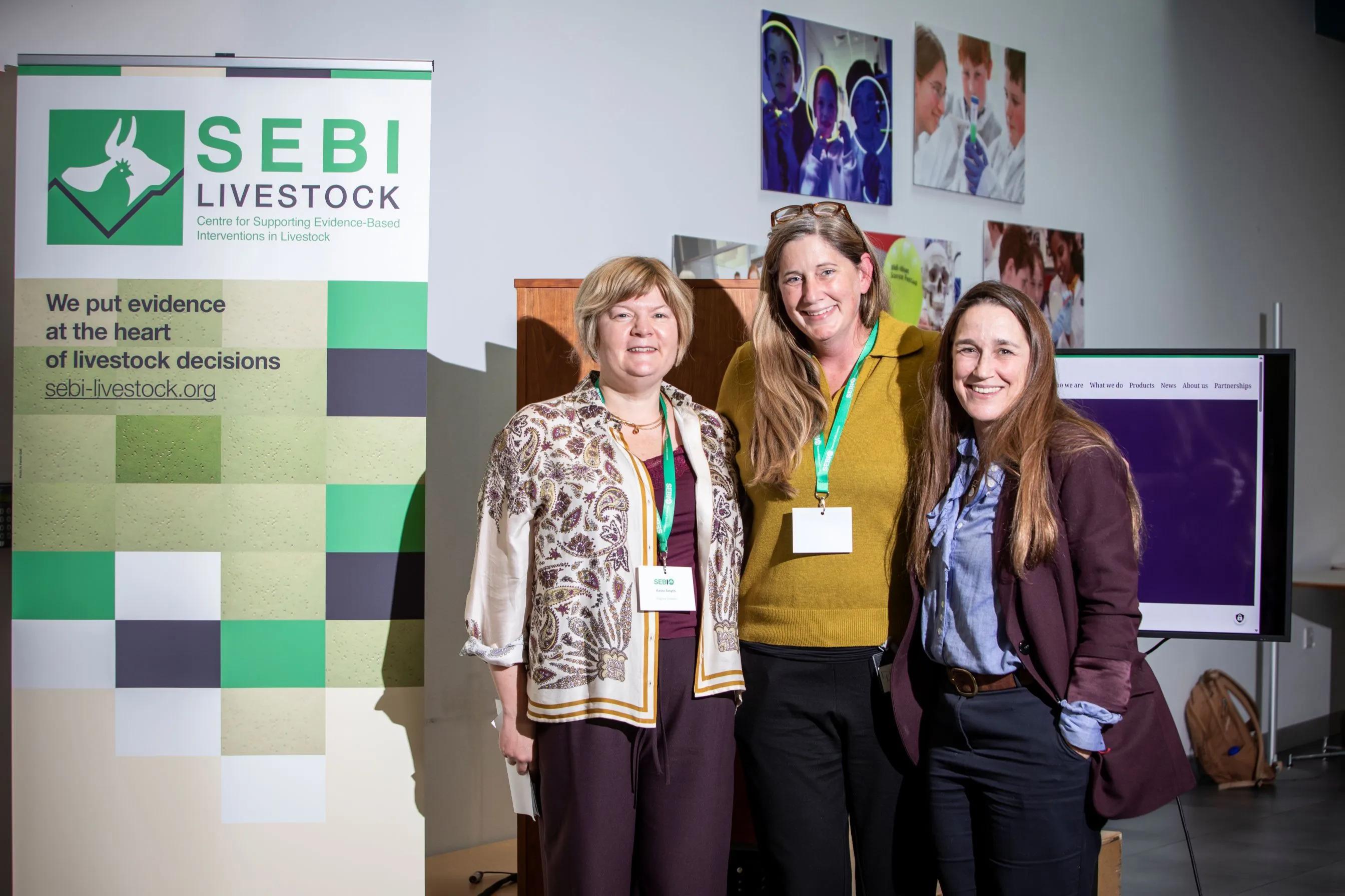 Three people in suits stand in front of a SEBI banner, smiling.