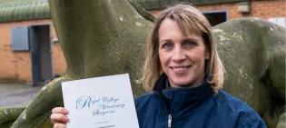 Image of DVE Practice Manager outside, smiling to camera and holding a certificate