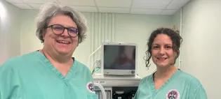 image of two females in green scrub tops standing next to an anaethesia machine and smailing to the camera