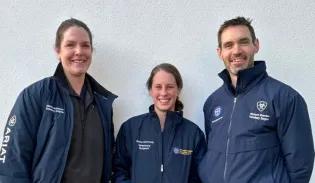 three people stand against a white backfriund, wearing blue outdoor jackets branded Dick Vet Equine Hospital