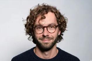 headshot of a man with long wavy hair, wearing glasses
