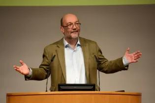 Professor Bruce Whitelaw stands at a podium with his arms outstretched.