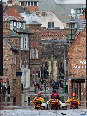 Rescuers with a boat and wading through the water of a flooded street in the middle of York city buildings