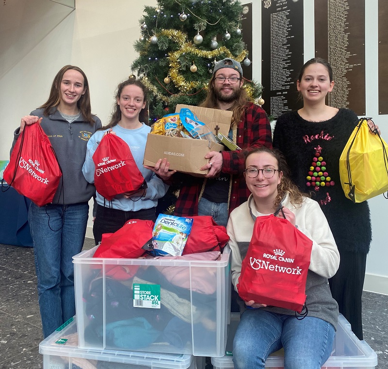 five students standing in front of a christmas tree with dozens of small filled bags 