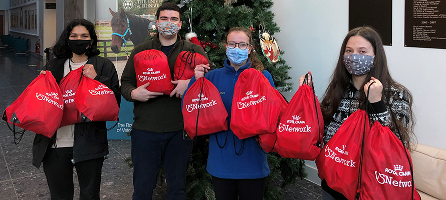 A group of students stands in front of a Christmas tree holding donation bags